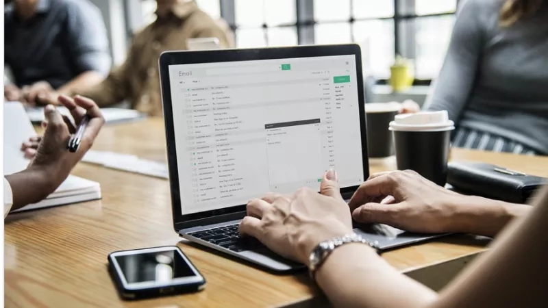 Woman typing on laptop with coworkers in background for article on organization.