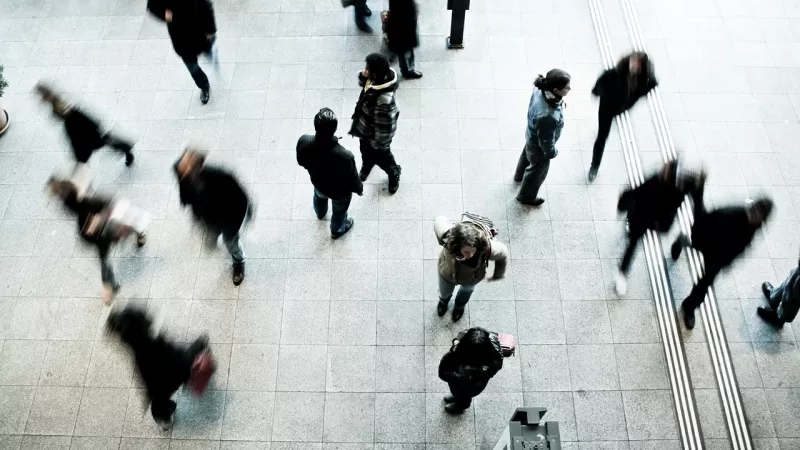 Pedestrians in a public area, many walking with a blurred effect, while two are clearly visible.