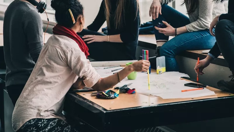 A group of people are working together on a project using pens, pencils, paper, and electronic devices.