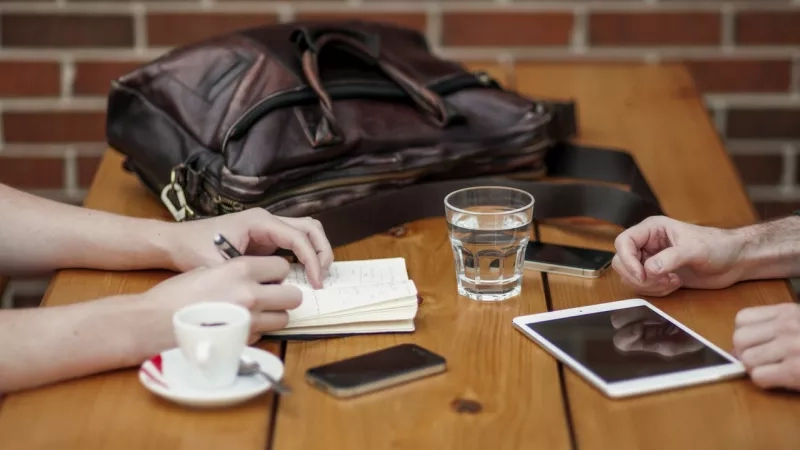 People sitting at a table with writing utensils and mobile phones, and a glass of water.