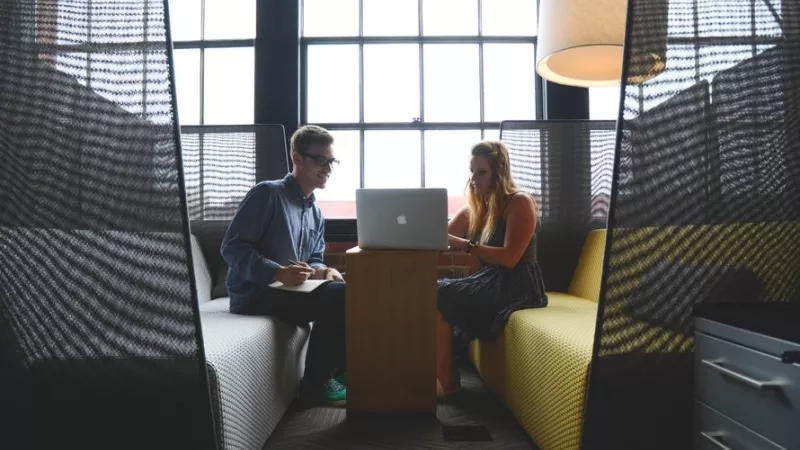 People working in a yellow-colored office, with a large window in the background.