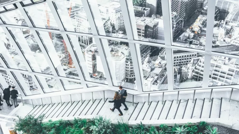 People walking in a hallway with glass windows in the background, showing the view of the city.