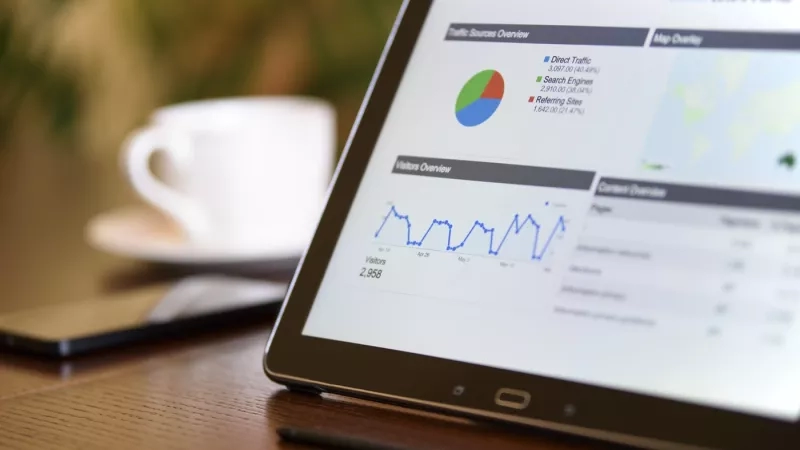 Tablet showing analytics with a cup of coffee and cellphone on a desk in a blurred background.