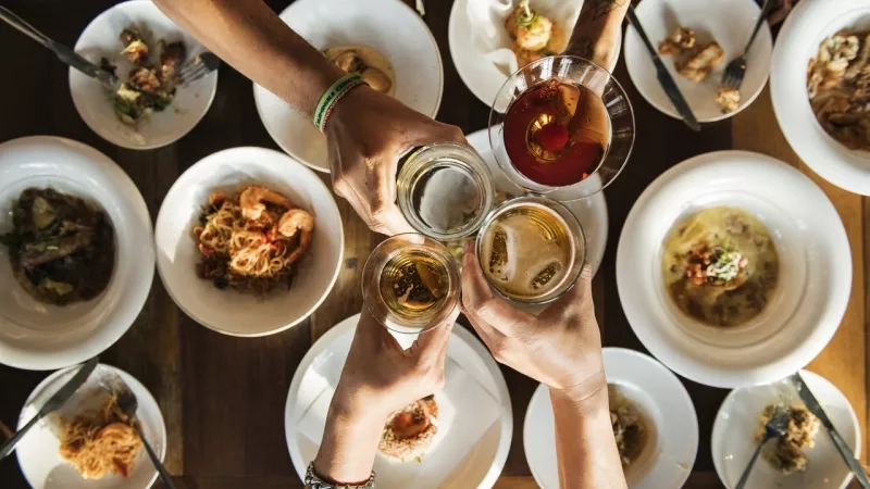 Hands with drinks raised in a toast over a table filled with plates of food at the hotel.