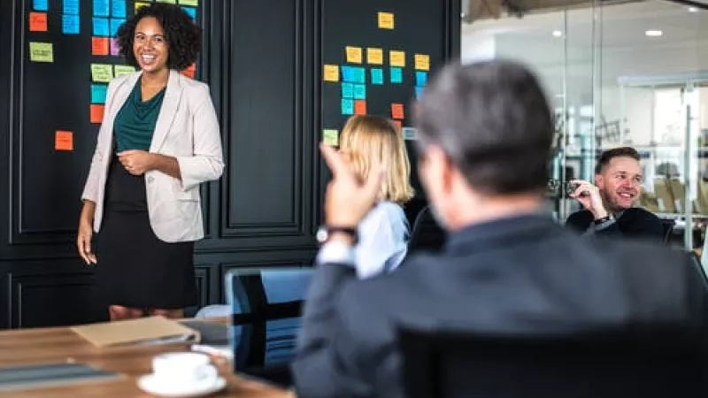 A woman is giving a presentation in a conference room with a group of people.