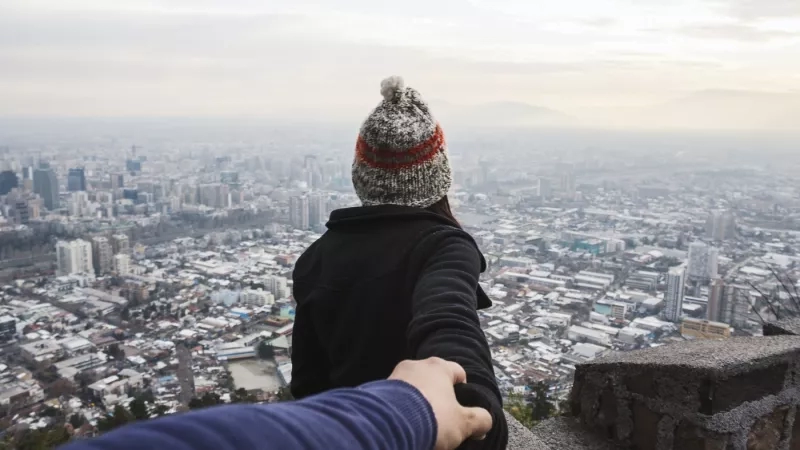 A person wearing a hat holding another persons hand while looking at a cityscape.