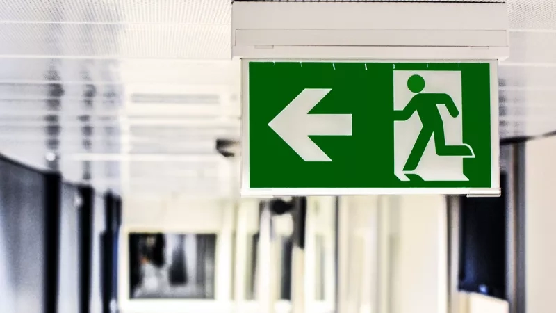 Emergency exit sign with a green background and a white arrow pointing to the left.