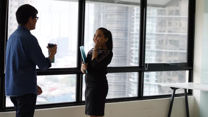 A man and a woman are standing in front of a glass window with a view of the city.