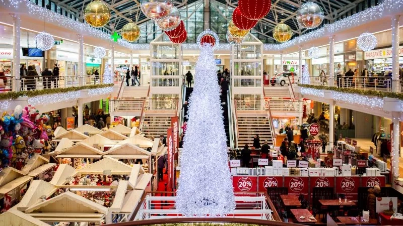 White Christmas tree in the middle of the mall with lots of people and stores around.