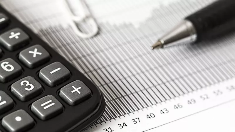 Calculator and pen on financial document with numbers 25, 28, 31, 34, 37, 40, 43, 46, 49, 52, 55.