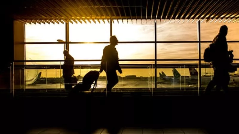 Silhouettes of travelers in an airport, with a sunset view through large windows, highlighting the vibrant ambiance.