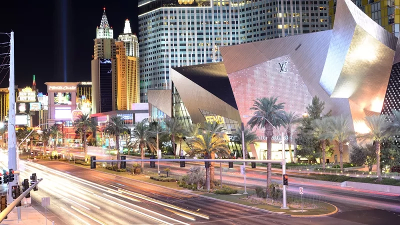 Night view of The Strip in Las Vegas with a Louis Vuitton building and palm trees on the side.