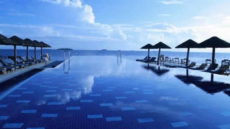 An empty swimming pool with chairs, umbrellas, and a view of the ocean on a sunny day.