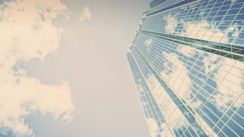 A tall building with glass windows reflects the blue sky and white clouds in the sky.