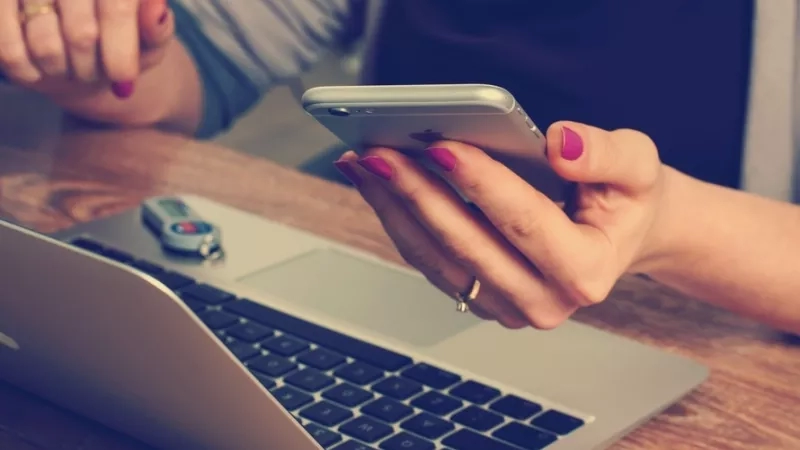 Person with smartphone and laptop working in cafe with 7 ways to reduce stress as a freelancer.