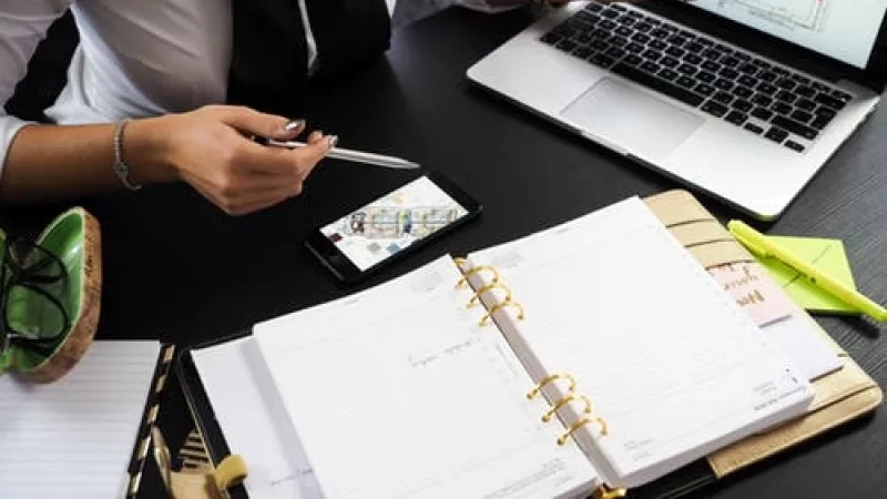 Businesswoman working on a laptop with architectural plans, surrounded by office supplies and a notebook.