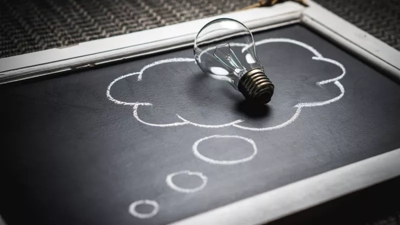 A blackboard with an image of a light bulb on top of a cloud drawn in chalk.