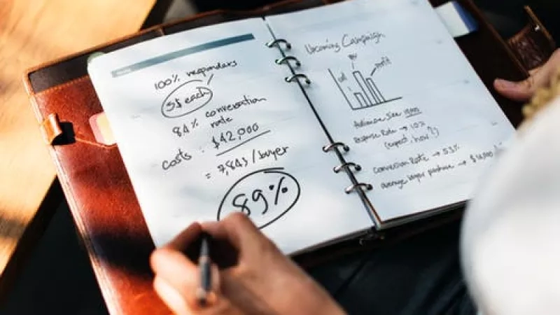 Person writing on a notebook with a pen about a marketing campaign with a 99% success rate.