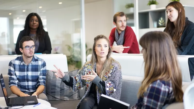 A group of people sitting around a table with laptops, having a meeting in an office.