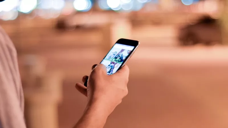 A person holding a cellphone, blurred background with lights, and the screen displaying a picture of two people.