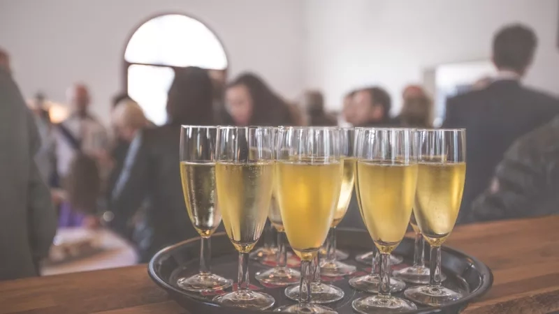 Glasses of champagne in a tray with a blurred crowd of people in the background.