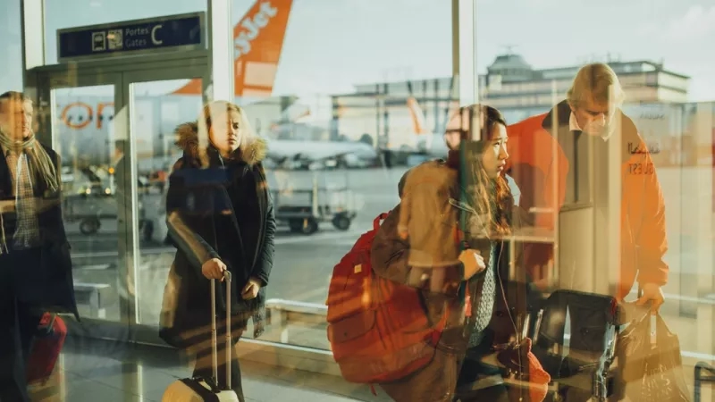 A group of people in an airport with their luggage and an airplane in the background.