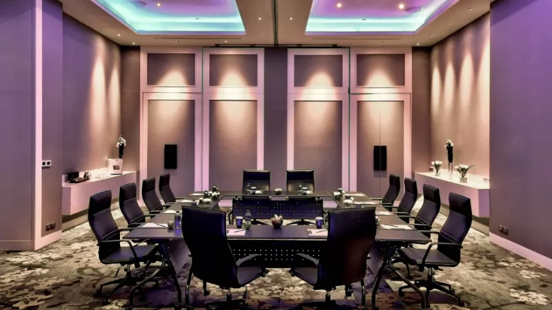 The conference room has chairs, a table, and a carpeted floor with a purple and blue ambiance.