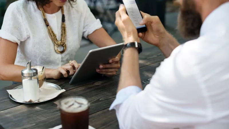 A man and a woman are using their cell phones while having coffee in a cafe.