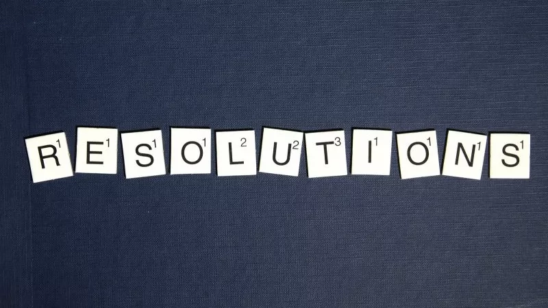 The word resolutions spelled out in Scrabble tiles on a blue background.