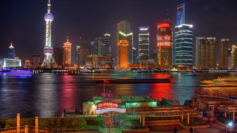 The illuminated Shanghai skyline at night with the Oriental Pearl Tower in the distance.