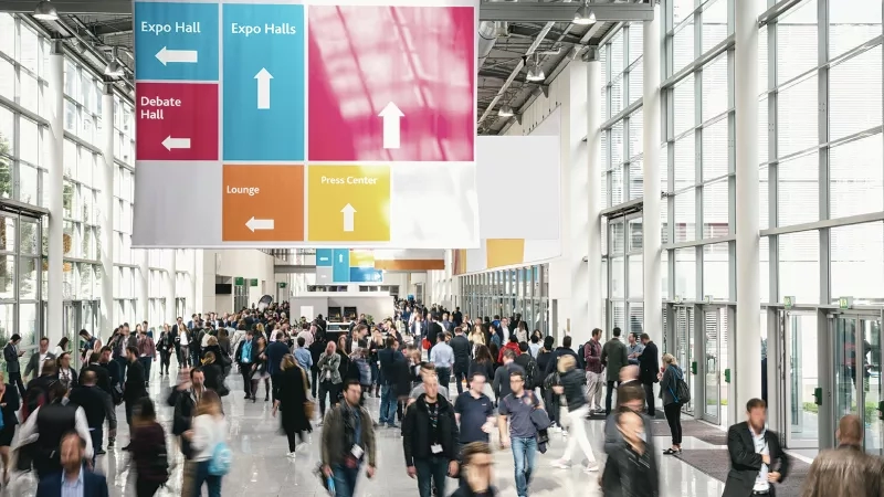 People at a conference with a banner that says "Expo Halls" and "Debate Hall" in the background.