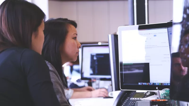 Two women working at desks in a modern office space with a lot of technology and computers.