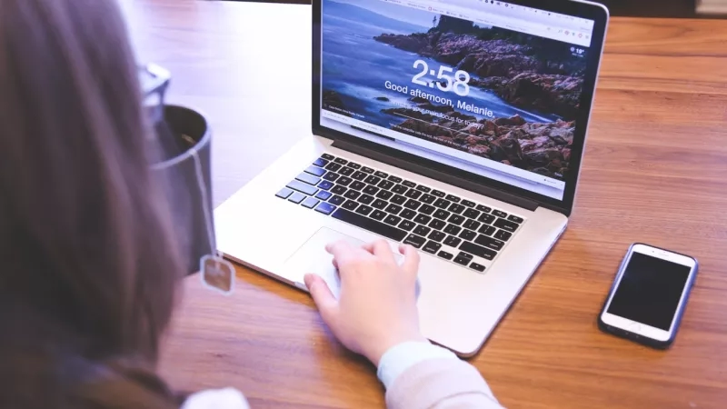 A woman using a laptop on a table with a smartphone next to her.