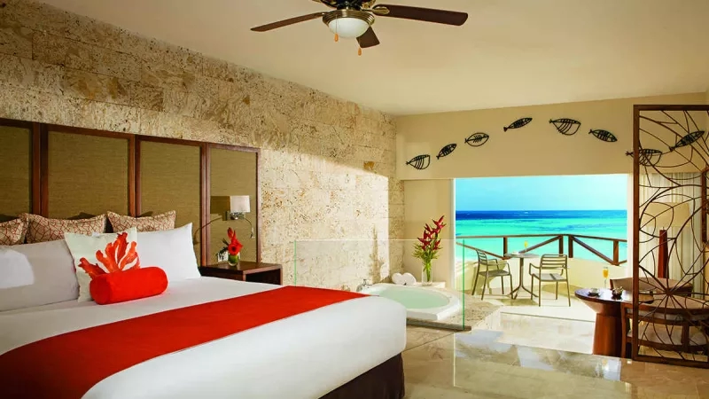A luxury hotel room with a king-sized bed, balcony, and whirlpool tub overlooking the ocean.