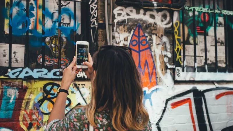 A woman taking a picture of graffiti on a wall with her smartphone.
