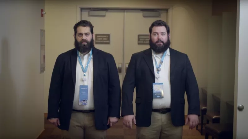Two bearded men stand next to each other in a hallway at the Dreamforce conference.
