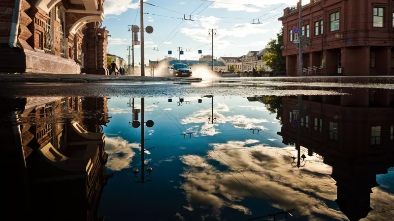 Car splashing through a puddle in the street with reflections of buildings in the water.