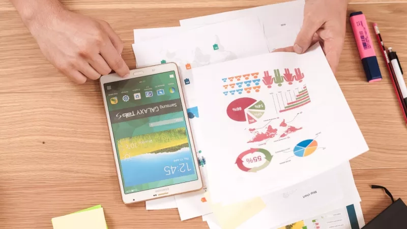 A person is using a Samsung tablet with papers and a pen nearby on a table.