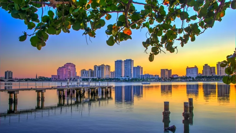 West Palm Beach skyline under seagrape tree at sunset in Florida, with a pier and calm water.