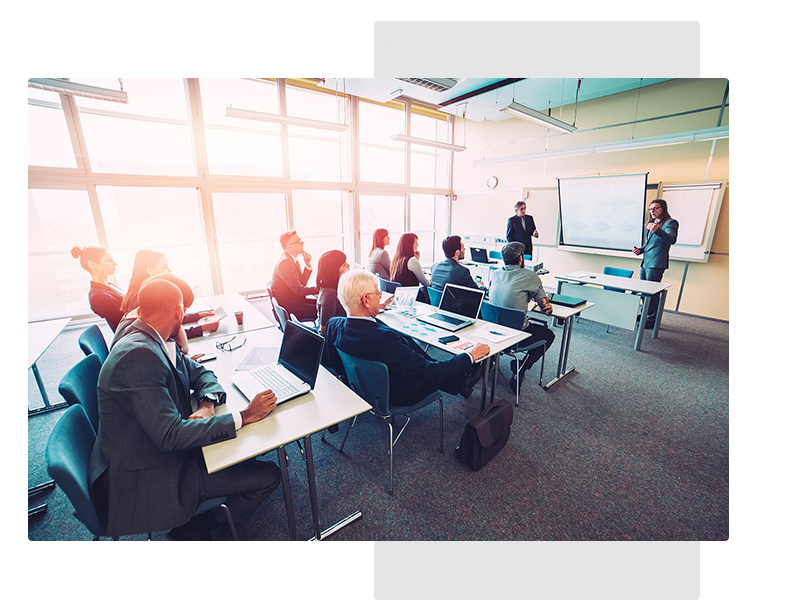 A group of people attending a meeting inside a classroom with glass windows and white walls.