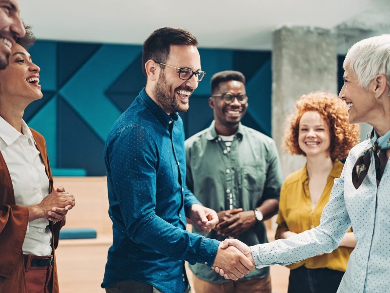 A group of diverse professionals are seen shaking hands and smiling in an office environment.