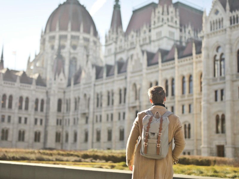 A man with a backpack is walking towards the Hungarian Parliament Building in Budapest, Hungary.