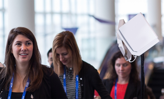 Three women with blue lanyards stand in front of an RFID reader at an event in a modern space.