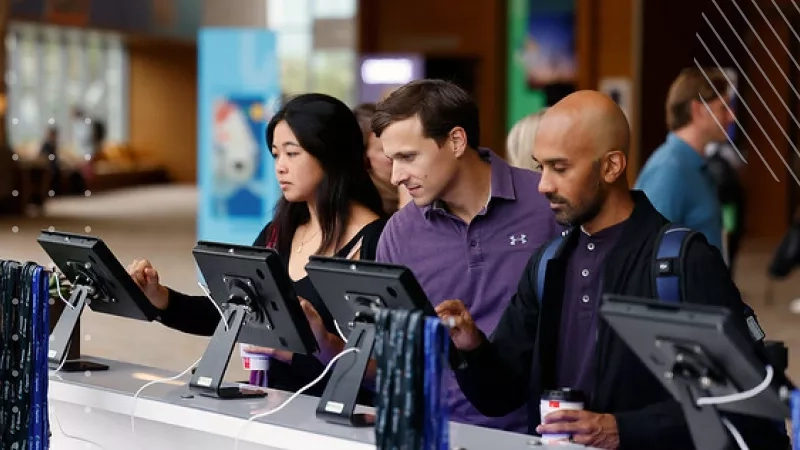 A group of people standing at a desk with monitors and a cup of coffee.